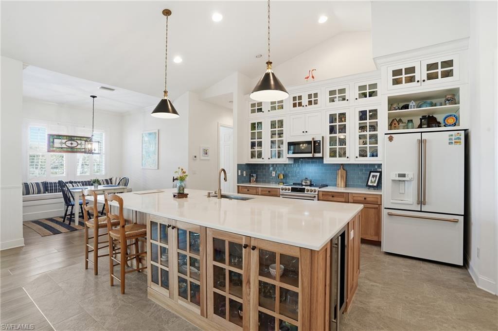 Image 3: Two tone kitchen featuring glass fronted cabinets, two tone cabinetry, hanging light fixtures, high end appliances, and a breakfast bar area