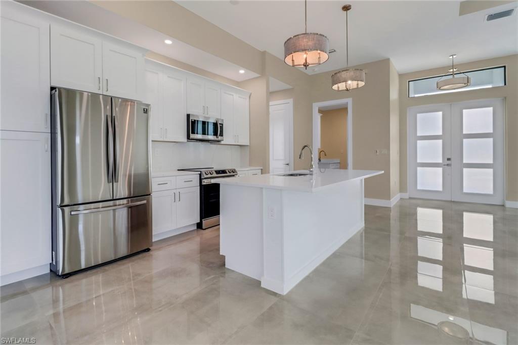 Image 4: Kitchen with stainless steel appliances, a kitchen island with sink, white cabinets, light countertops, and hanging light fixtures