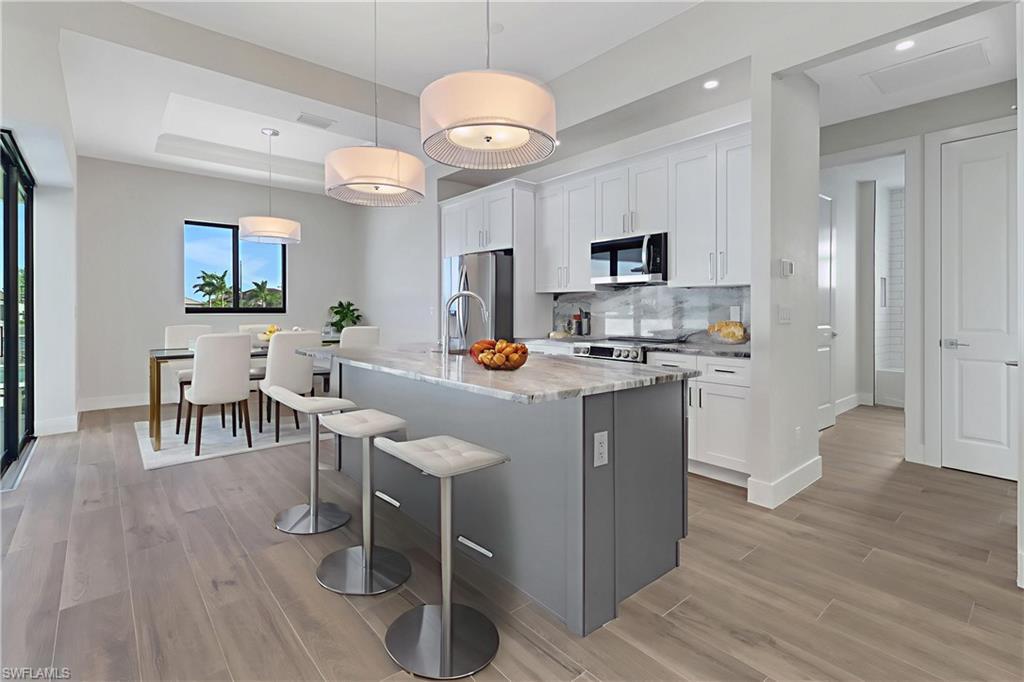 Image 4: Kitchen with freestanding refrigerator, a raised ceiling, a center island with sink, light wood-type flooring, and recessed lighting
