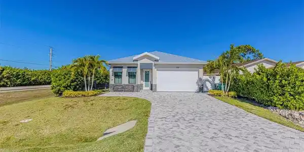 Image 2: Single story home with a front lawn, decorative driveway, an attached garage, stone siding, and a metal roof