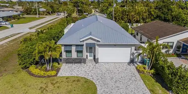 Image 3: Ranch-style house featuring decorative driveway, a garage, a front lawn, a metal roof, and view of scattered trees