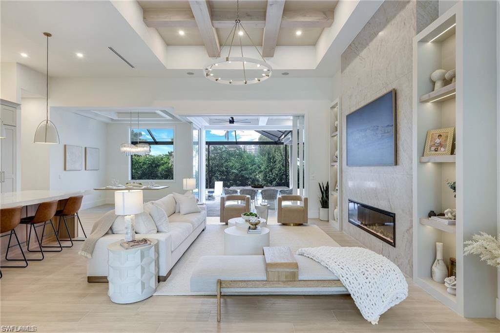 Image 2: Living room with built in shelves, a large fireplace, coffered ceiling, light wood finished floors, and recessed lighting