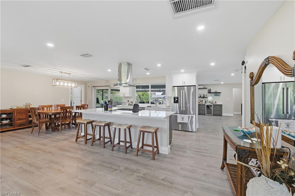 Image 2: Open Concept Kitchen with stainless steel refrigerator with ice dispenser, light quartz counters, LVP floors, wine cooler, and white cabinetry