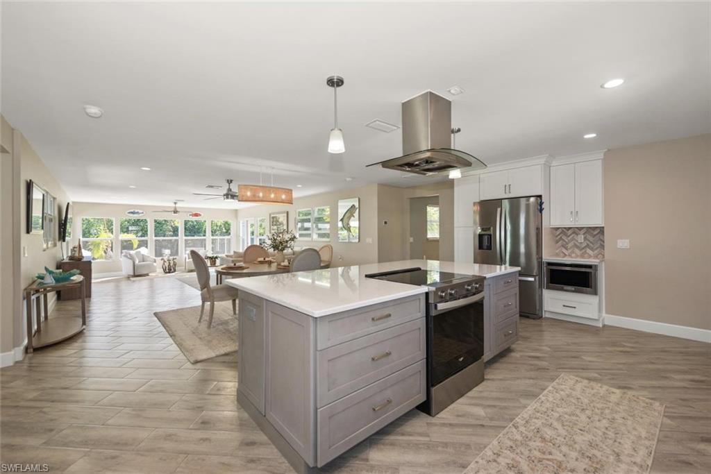 Image 4: Dual tone kitchen with two tone cabinetry, stainless steel appliances, island range hood, open floor plan, and wood finish floors