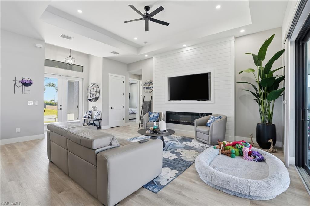 Image 4: Living area featuring a ceiling fan, light wood finished floors, a raised ceiling, a glass covered fireplace, and recessed lighting