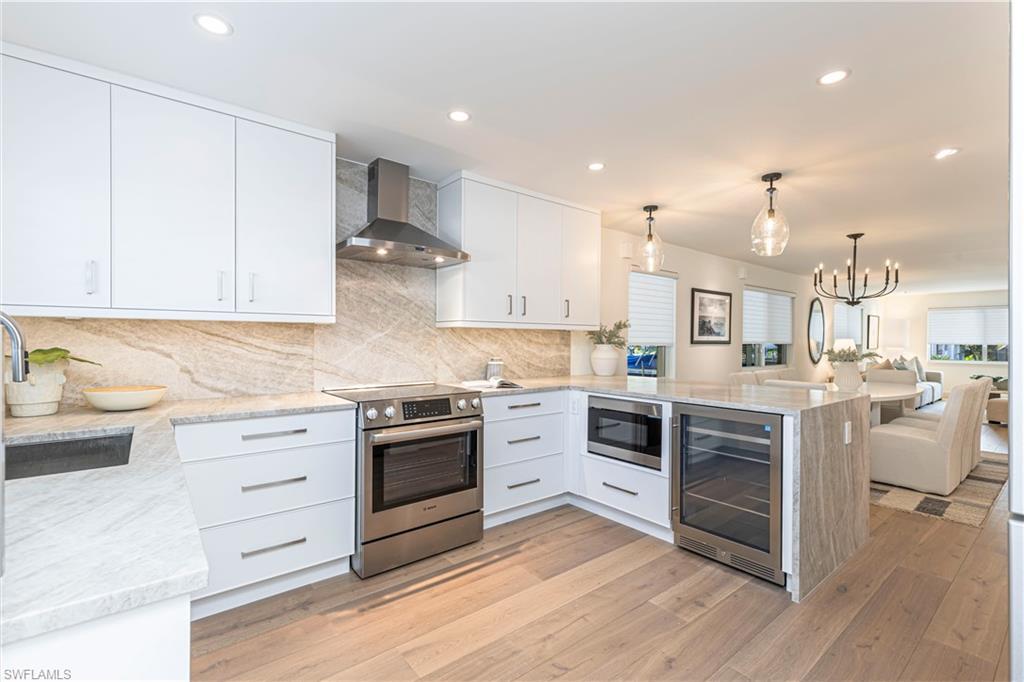 Image 2: Kitchen with beverage cooler, wall chimney exhaust hood, appliances with stainless steel finishes, open floor plan, and a peninsula