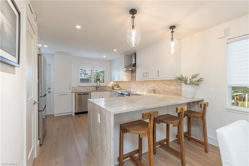 Image 3: Kitchen featuring stainless steel appliances, a peninsula, white cabinets, wall chimney range hood, and pendant lighting