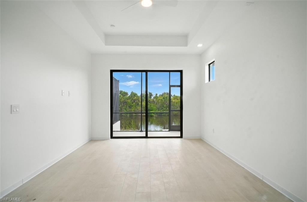 Image 4: Unfurnished room featuring light wood-style flooring, ceiling fan, a water view, and a raised ceiling
