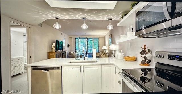 Image 4: Kitchen with stainless steel appliances, a peninsula, white cabinets, and hanging light fixtures