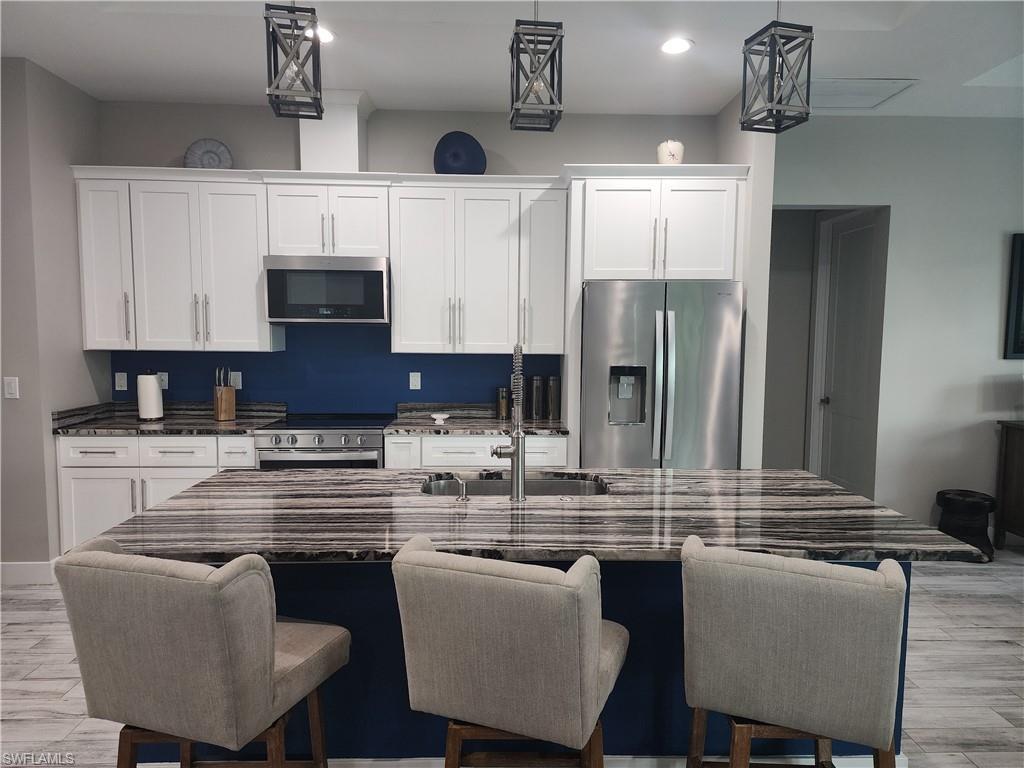 Image 4: Kitchen featuring white cabinetry, appliances with stainless steel finishes, an 8ft 4in island, and pendent lighting