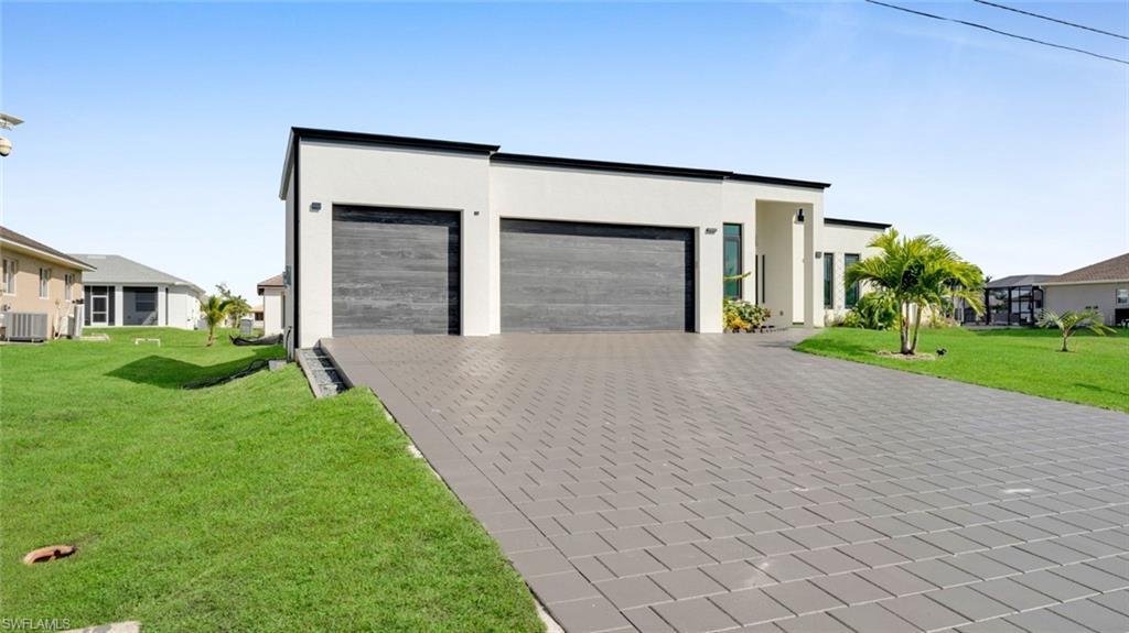 Image 4: Modern home with a front yard, decorative driveway, an attached garage, and stucco siding