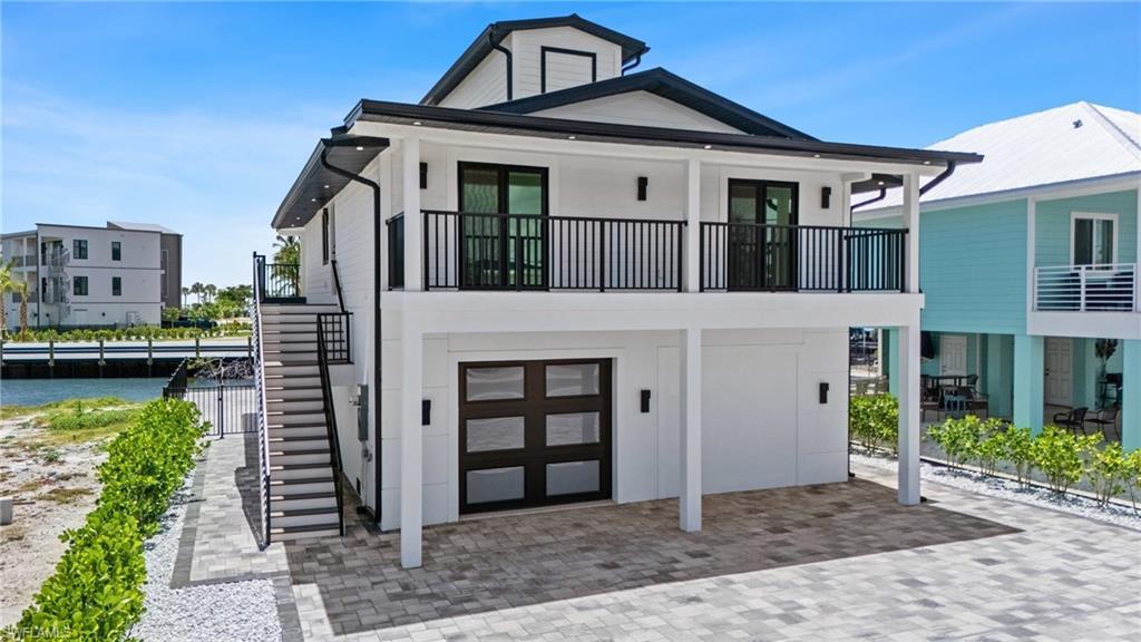Image 1: Coastal home with stairs, an attached garage, a water view, and a balcony- Virtually Edited