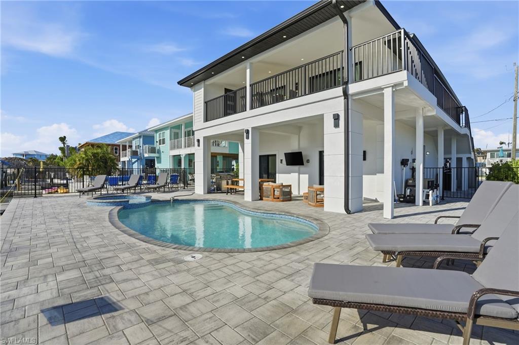 Image 2: Back of property featuring a patio area, a pool with connected hot tub, a balcony, and an outdoor hangout area Virtually Edited