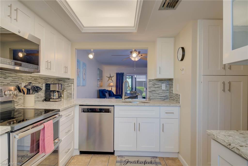 Image 2: Kitchen featuring stainless steel appliances, white cabinetry, light tile patterned floors, and backsplash