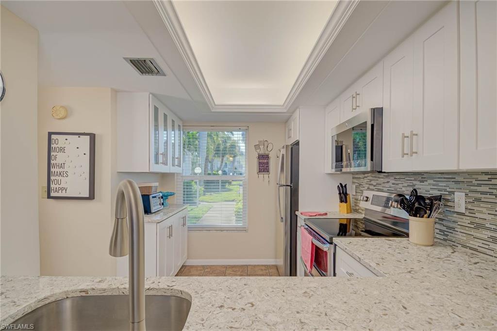 Image 4: Kitchen with white cabinetry, stainless steel appliances, light stone counters, a tray ceiling, and decorative backsplash