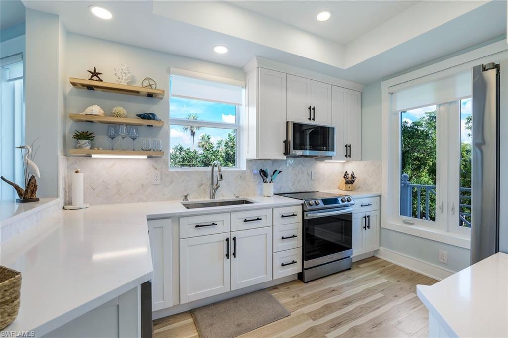 Image 1: Kitchen featuring white cabinetry, tasteful backsplash, appliances with stainless steel finishes, open shelves, and light wood-style floors