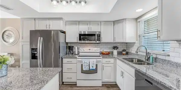 Image 2: The kitchen offers white shaker-style cabinetry, stainless steel appliances, a center island, granite countertops, new lighting, and a classic subway tile backsplash.