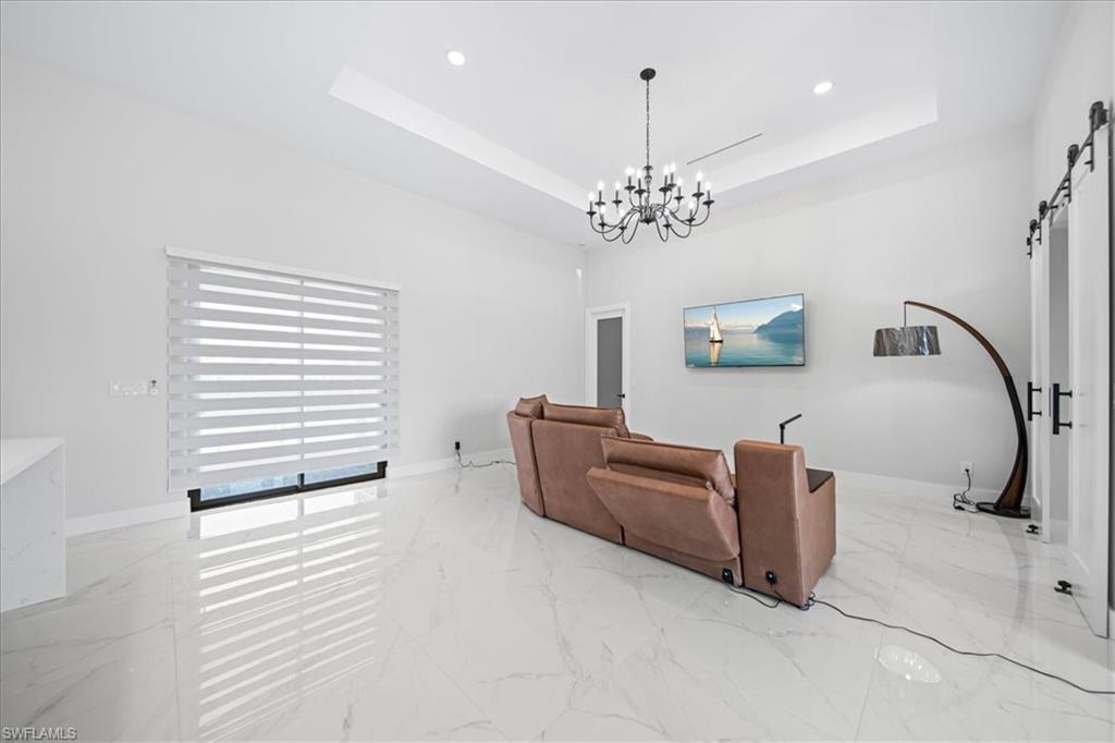 Image 4: Living area with a barn door, light marble finish flooring, hanging lights, and a raised ceiling