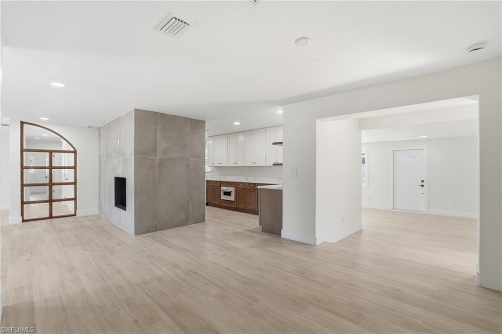 Image 4: Unfurnished living room featuring light wood finished floors, a tiled fireplace, and recessed lighting