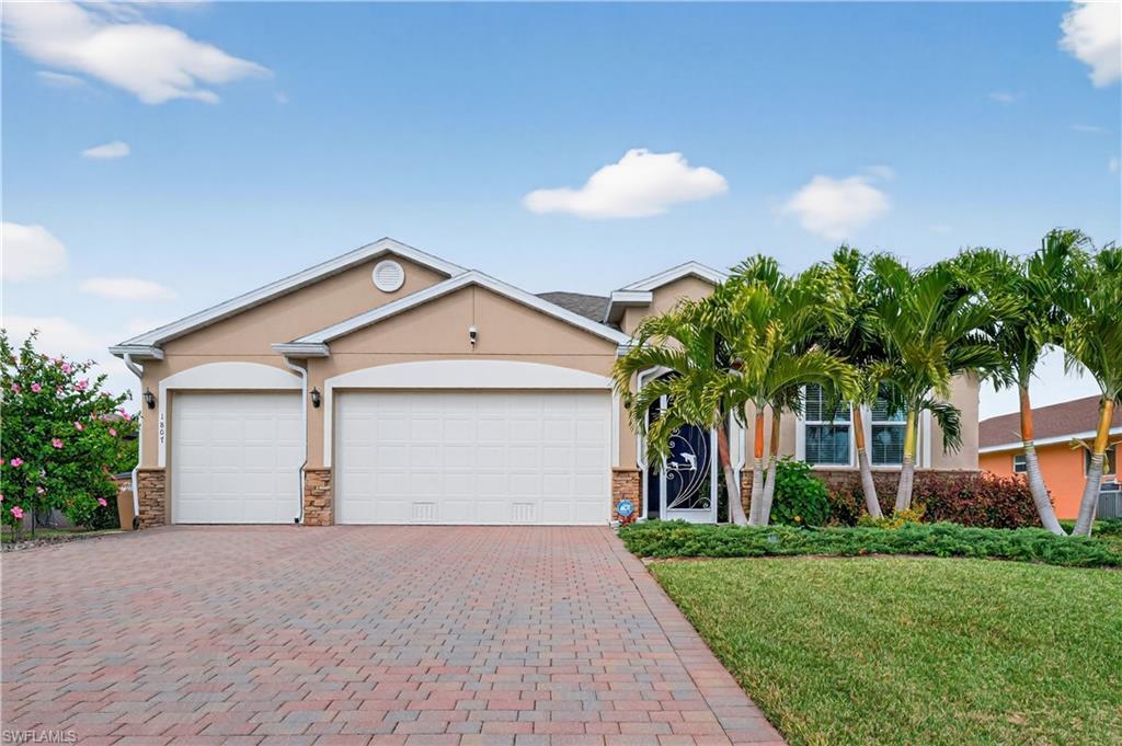 Image 2: Look at the lush Hibiscus,well manicured yard,featuring stucco siding, a front lawn, stone siding, decorative pavers driveway, and a 3 car garage