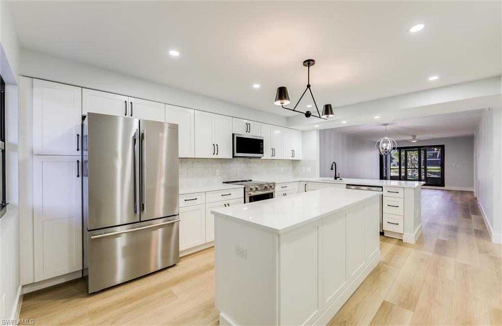 Image 2: Kitchen with stainless steel appliances, suspended lighting, light wood-type flooring, a peninsula, and white cabinetry