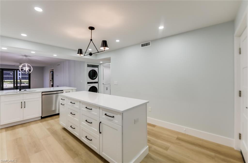 Image 3: Kitchen with stacked washer / dryer, stainless steel dishwasher, white cabinetry, light wood-type flooring, and a chandelier