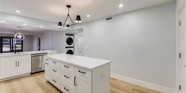 Image 3: Kitchen with stacked washer / dryer, stainless steel dishwasher, white cabinetry, light wood-type flooring, and a chandelier