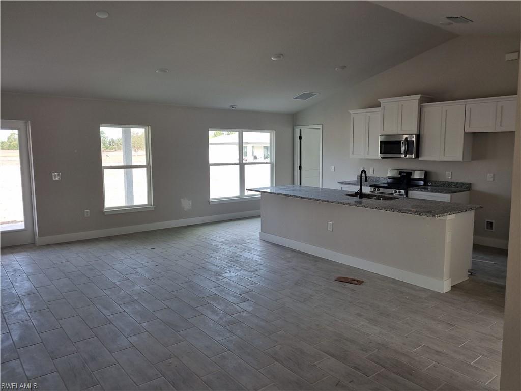 Image 4: Kitchen with dark stone countertops, an island with sink, stainless steel appliances, white cabinets, and wood tiled floors