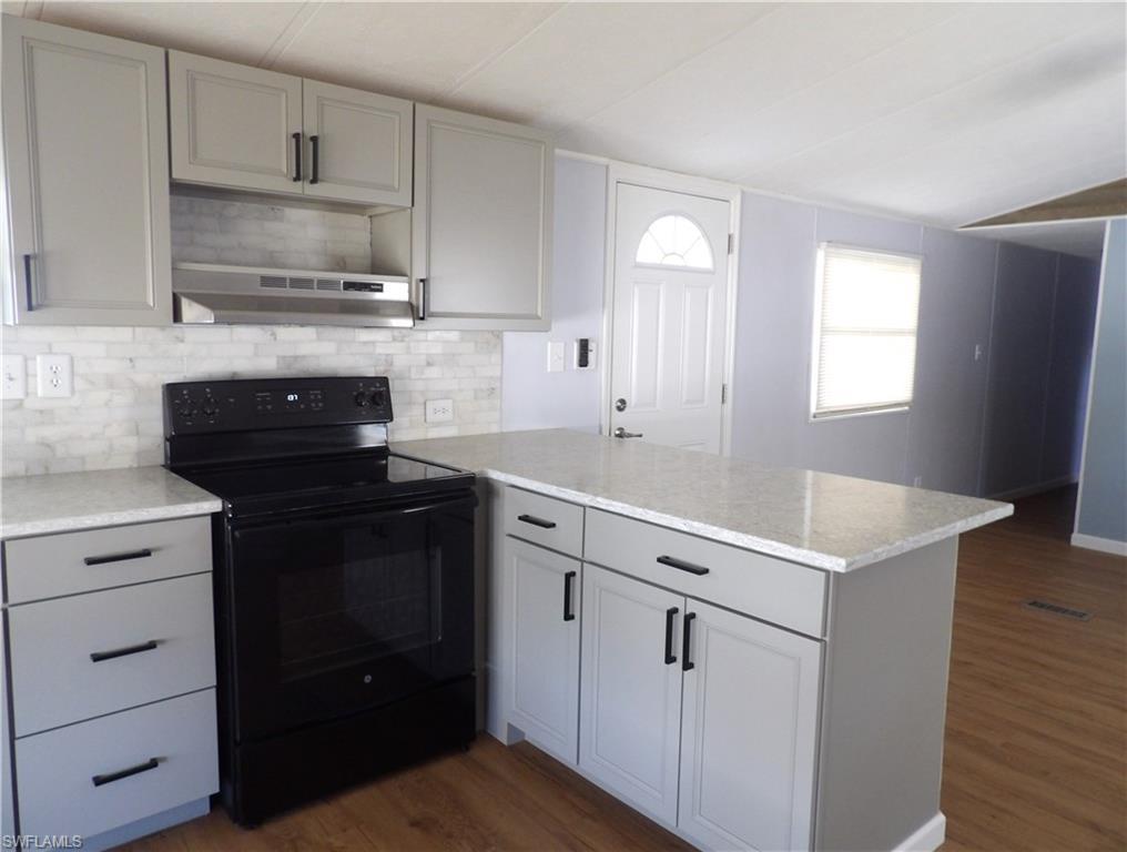 Image 3: Open Kitchen with black / electric stove, a peninsula, laminated finished floors, tasteful backsplash, and light stone counters