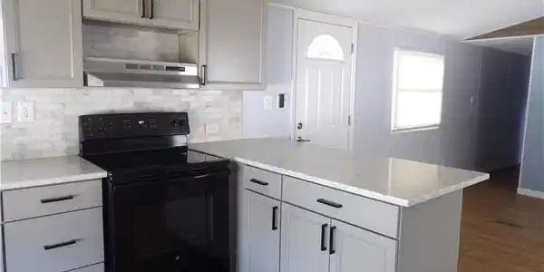 Image 3: Open Kitchen with black / electric stove, a peninsula, laminated finished floors, tasteful backsplash, and light stone counters