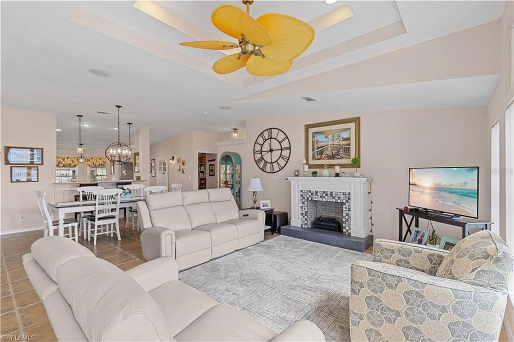 Image 4: Tiled living area with a tiled fireplace, ceiling fan, a chandelier, and a tray ceiling