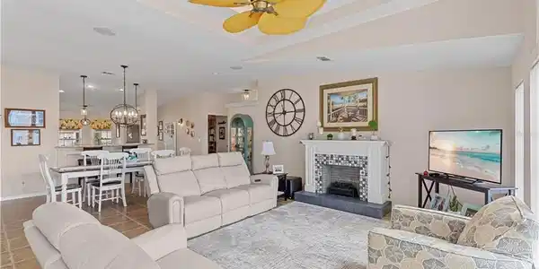 Image 4: Tiled living area with a tiled fireplace, ceiling fan, a chandelier, and a tray ceiling