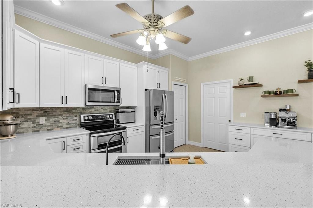 Image 4: Kitchen with stainless steel appliances, white cabinetry, light stone quartz counters, a ceiling fan, and crown molding