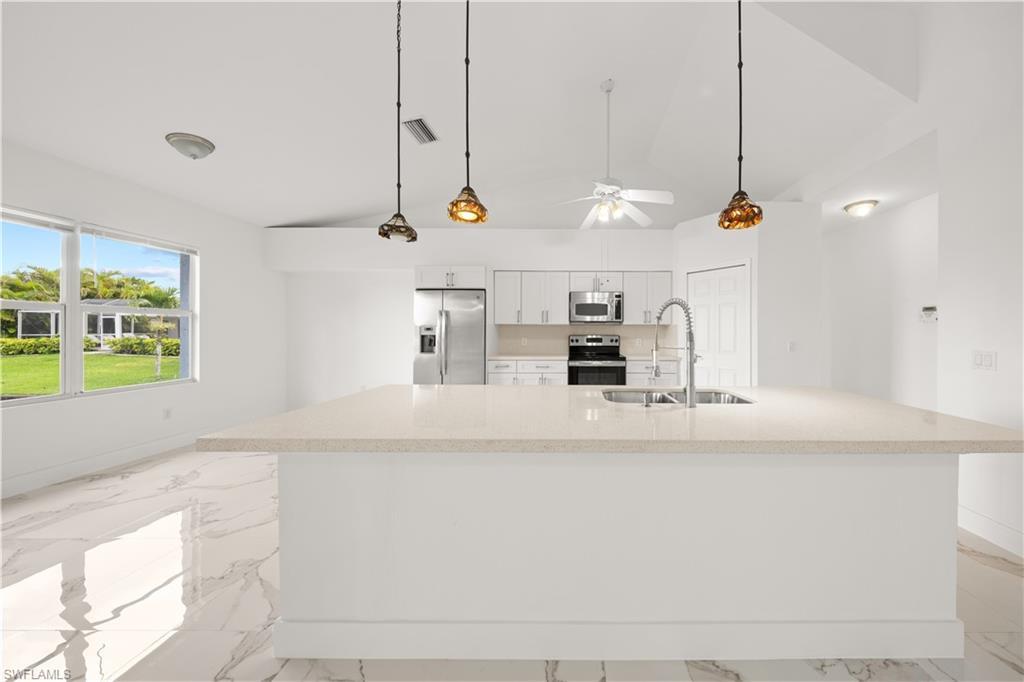 Image 1: Kitchen featuring white cabinetry, stainless steel appliances, decorative light fixtures, light marble finish flooring, and lofted ceiling