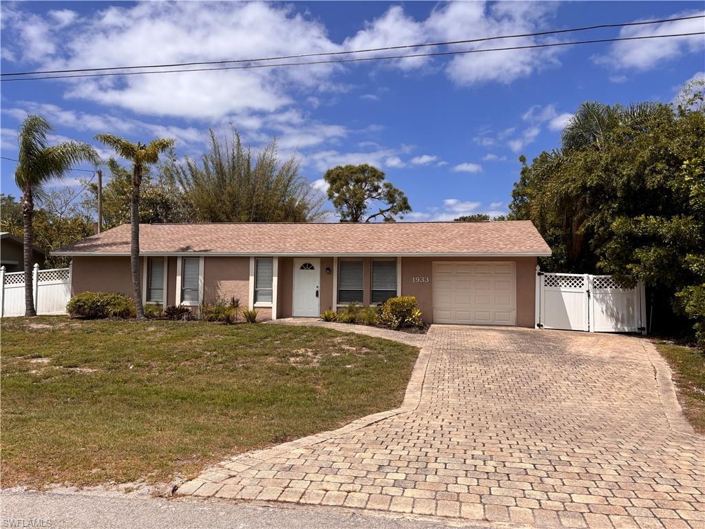Image 1: The property features a well-maintained exterior with a paved driveway, a white privacy fence, and mature palm trees