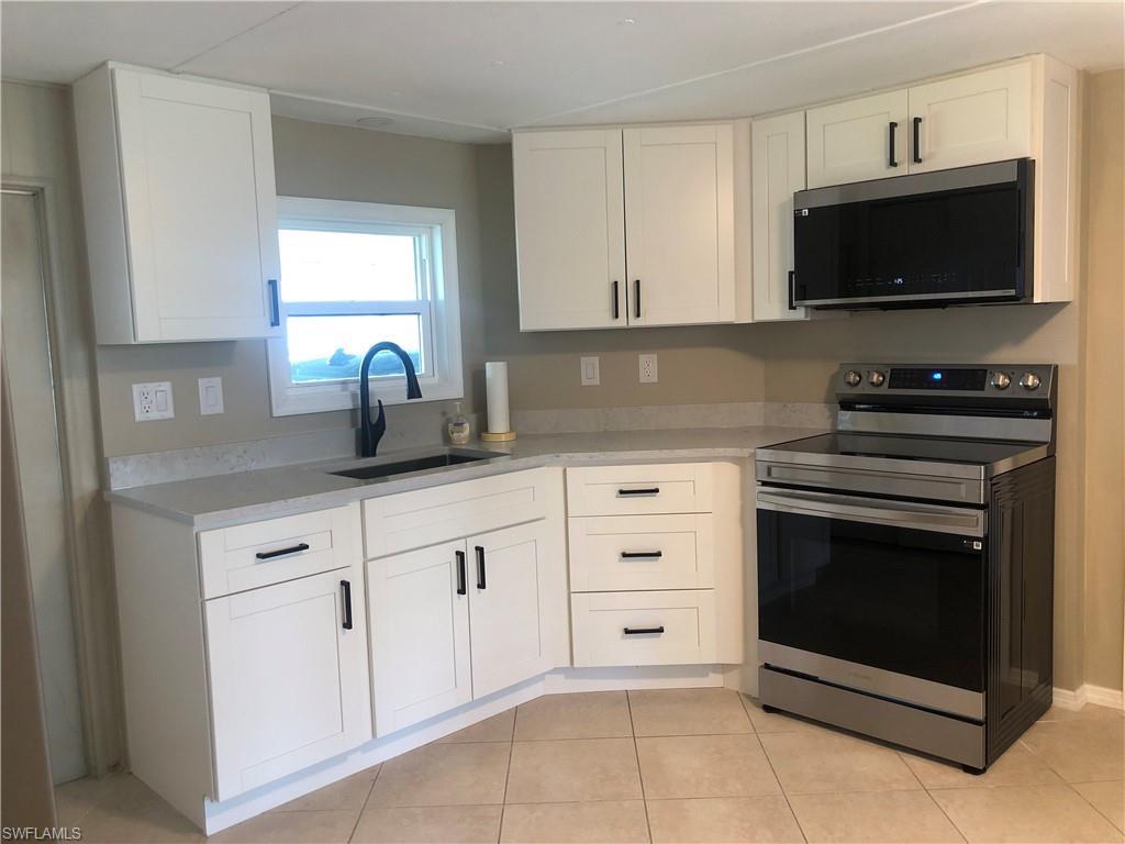 Image 1: Kitchen featuring sink, light tile patterned floor, quartz countertops, appliances with stainless steel finishes, and white cabinets