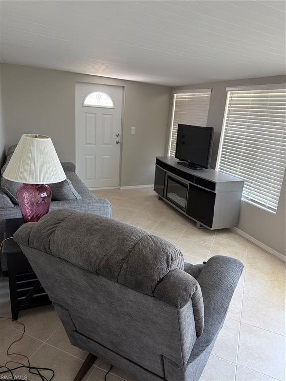 Image 4: Living area featuring a white entry door with an arched glass insert, two windows with horizontal blinds, light tile flooring, and light gray wall paint