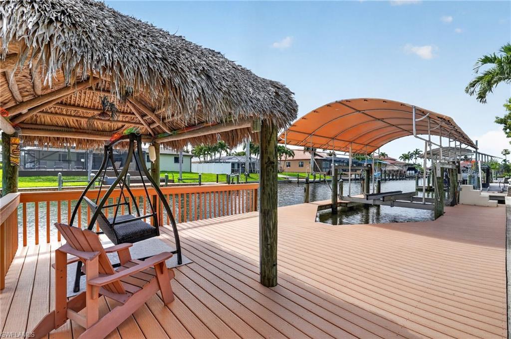 Image 3: Expansive waterfront deck featuring a thatched-roof tiki hut, dedicated boat lift with canopy, composite wood decking, and a wood railing system