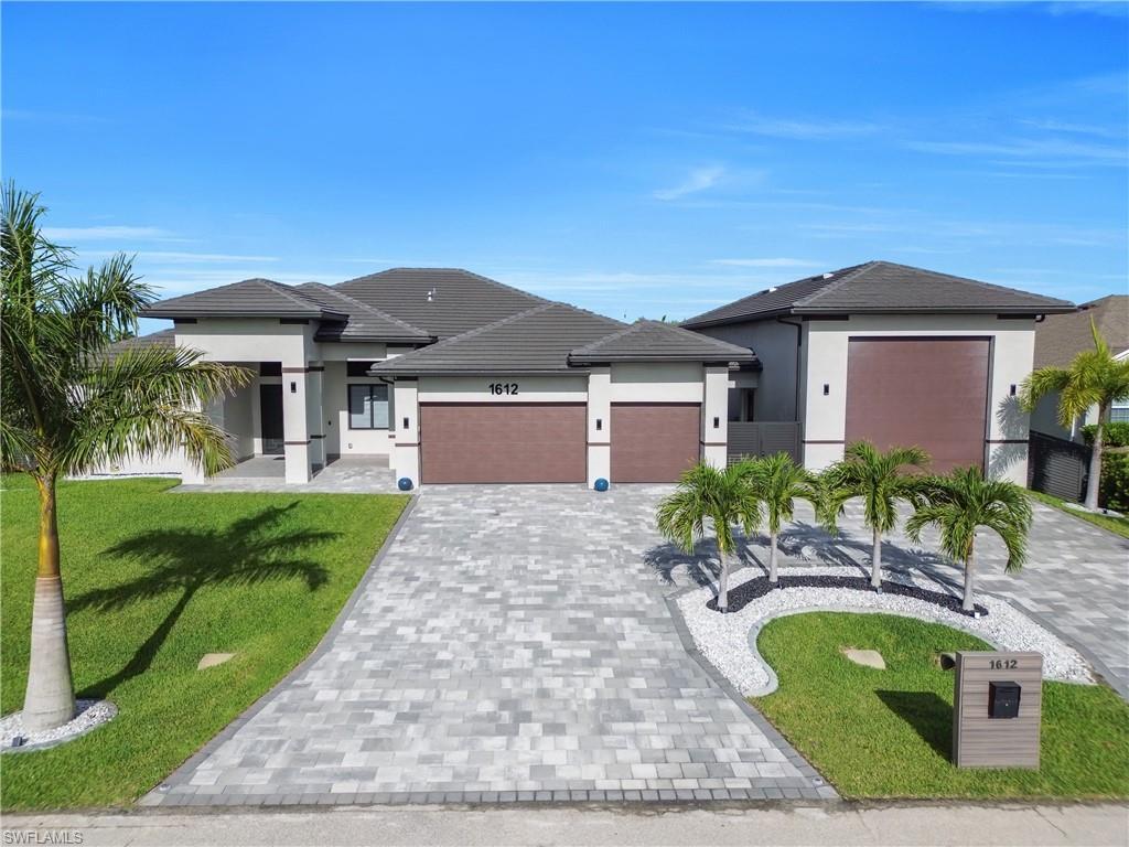 Image 1: Contemporary-style residence featuring a multi-car paved driveway, a tile roof, stucco exterior, and dual garage doors