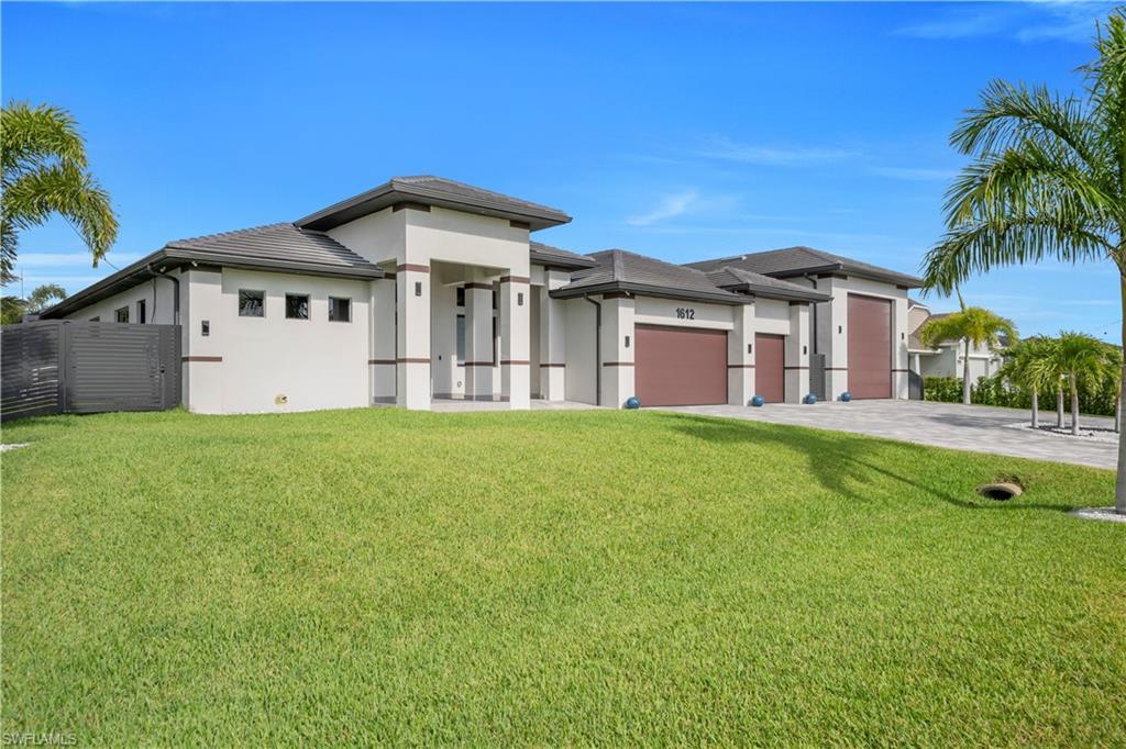 Image 2: Modern stucco exterior featuring a flat tile roof, three brown garage doors, a paver driveway, and a spacious front lawn