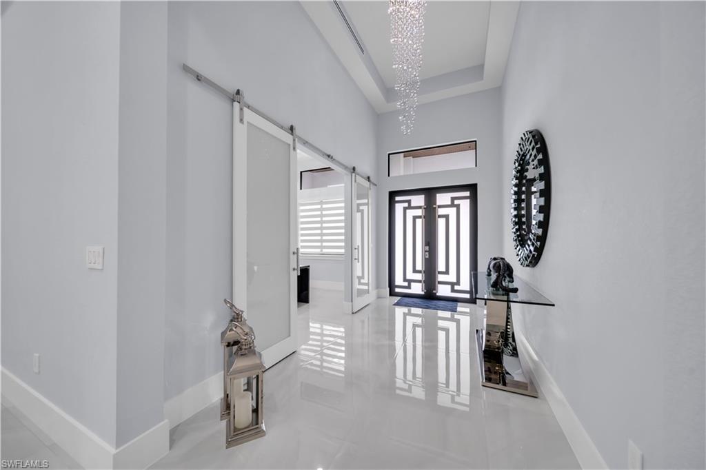 Image 4: Grand entryway featuring a double-door entrance with geometric detailing, high ceilings with a crystal chandelier, and large format tile flooring