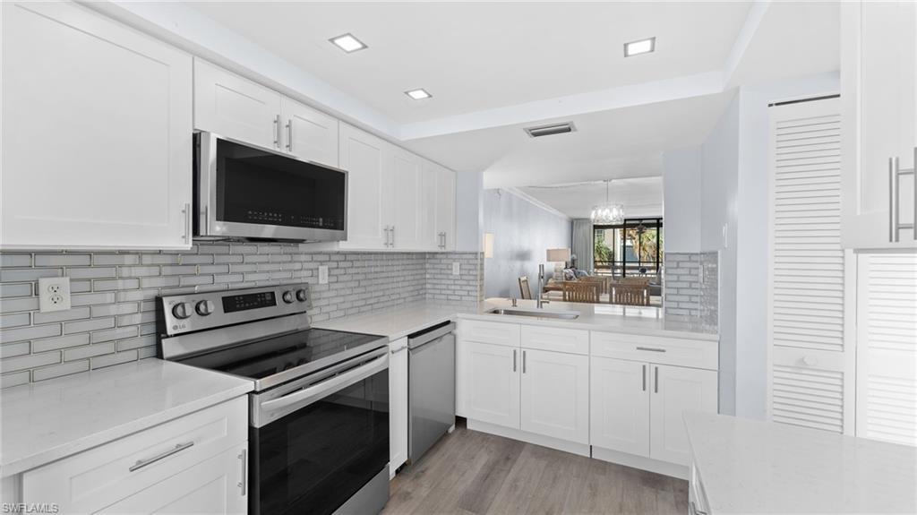Image 3: Kitchen with appliances with stainless steel finishes, white cabinetry, light stone counters, and backsplash
