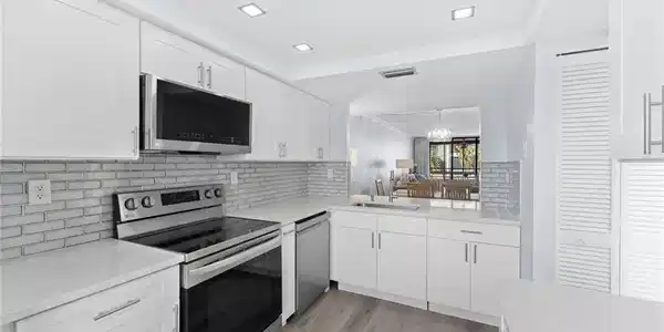 Image 3: Kitchen with appliances with stainless steel finishes, white cabinetry, light stone counters, and backsplash
