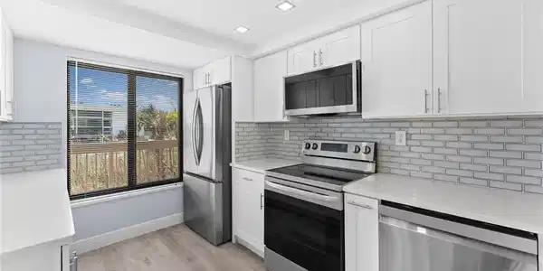 Image 4: Kitchen featuring appliances with stainless steel finishes, light stone counters, white cabinets, and tasteful backsplash