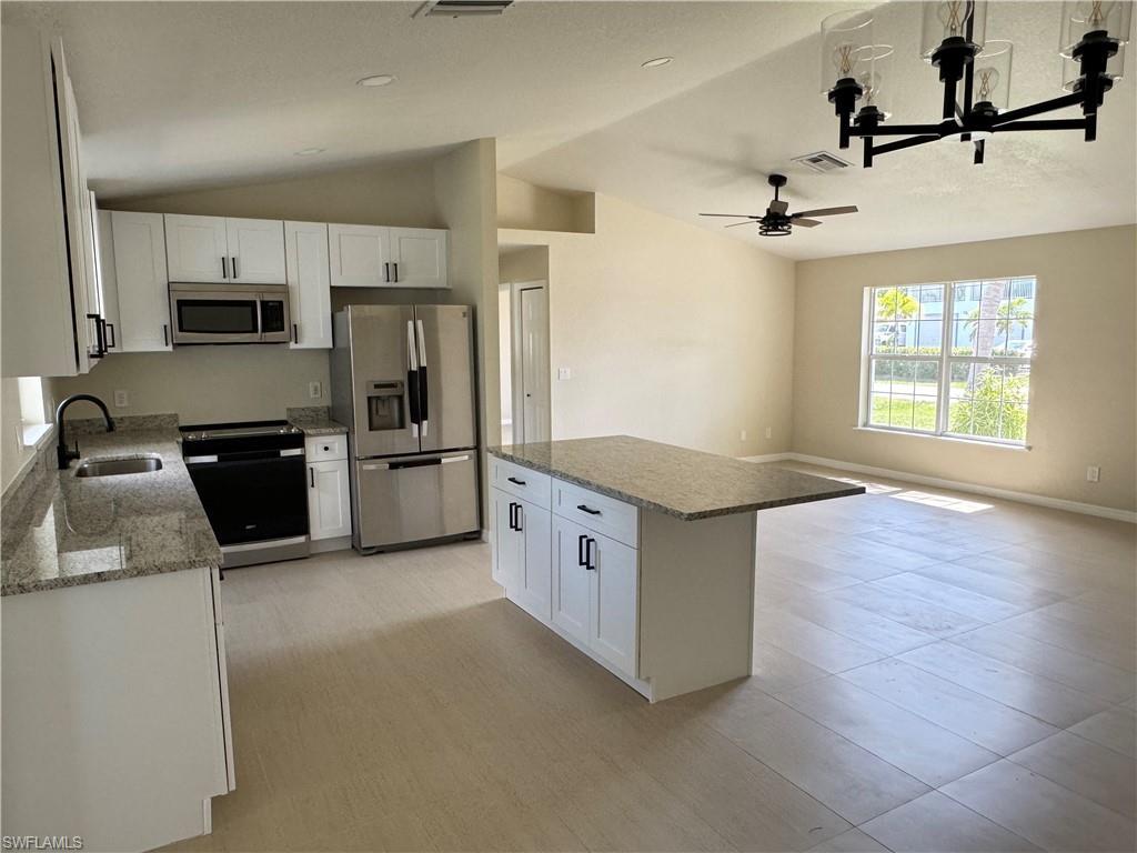 Image 3: Open-concept kitchen featuring white soft close cabinetry with black hardware, stainless steel appliances, granite countertops, and an island with a breakfast bar extension