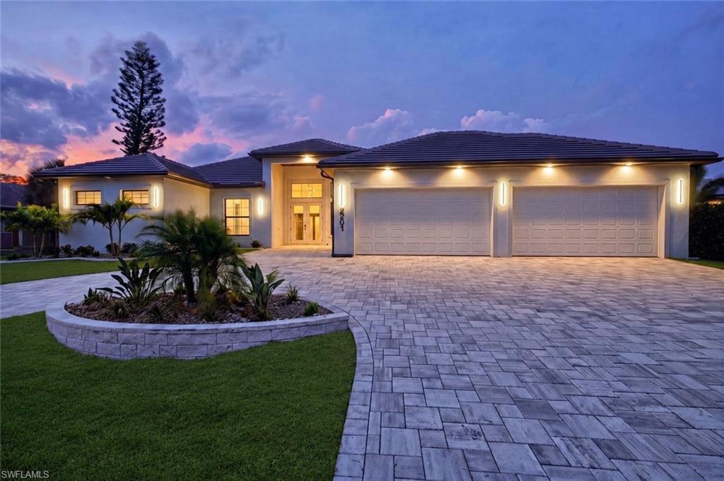 Image 2: Mediterranean-style exterior featuring a paved driveway, two-car garage, manicured lawn, and a stone-clad planter with landscaping