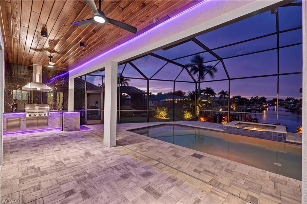 Image 4: Screened outdoor living area featuring a built-in outdoor kitchen with stainless steel appliances, wood-finish plank ceiling, and recessed lighting
