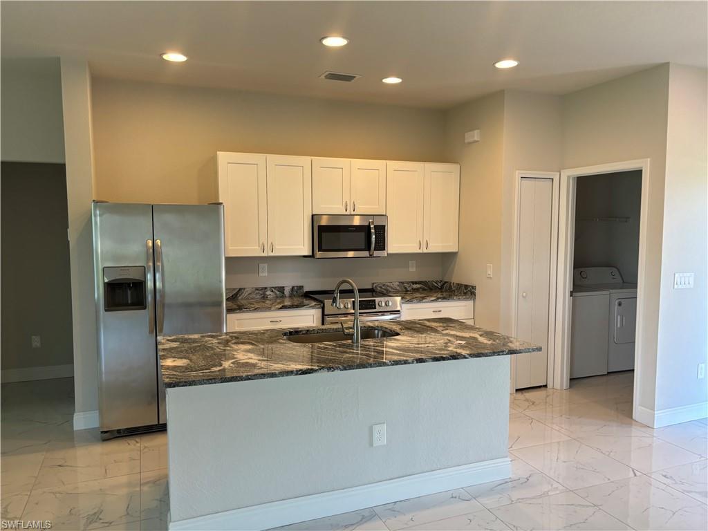 Image 1: Kitchen featuring dark stone counters, a kitchen island with sink, washer and dryer, appliances with stainless steel finishes, and sink