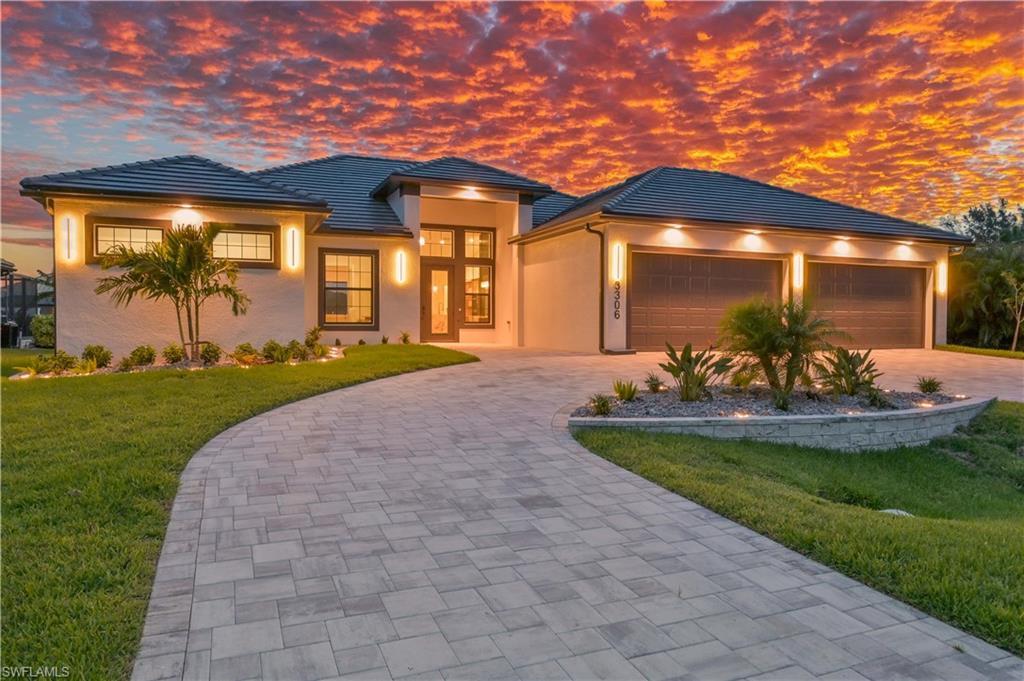 Image 2: Contemporary stucco exterior featuring a two-car garage with overhead lighting, a paver driveway, manicured landscaping, and a tiled roof
