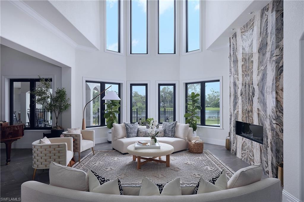 Image 3: Contemporary living area featuring a two-story ceiling, multiple large windows with black frames, a statement fireplace with a stone-finish facade, and recessed ceiling lights